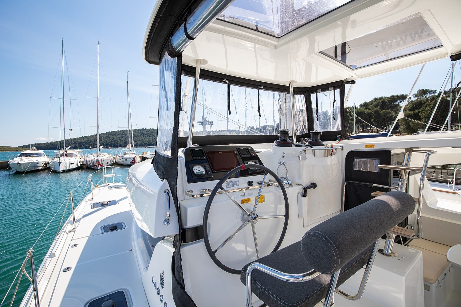 Helm station of the Lagoon 42 with wheel, chartplotter and winches under the enclosed bimini