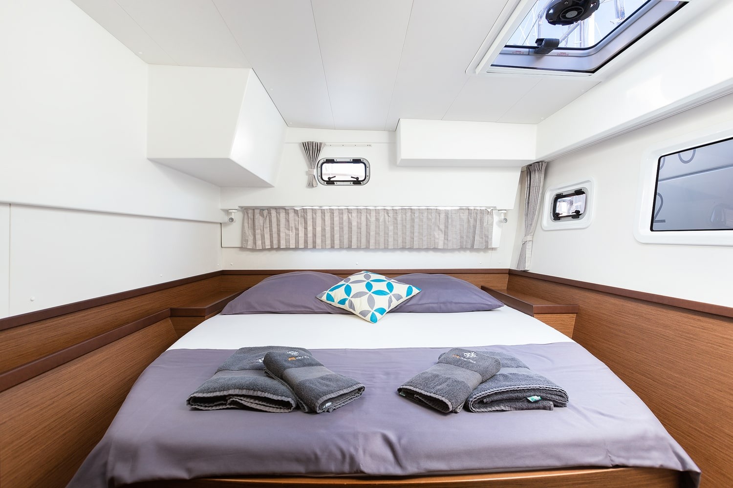 Double cabin in one hull of the Lagoon 42, bed made up with towels beneath an overhead hatch