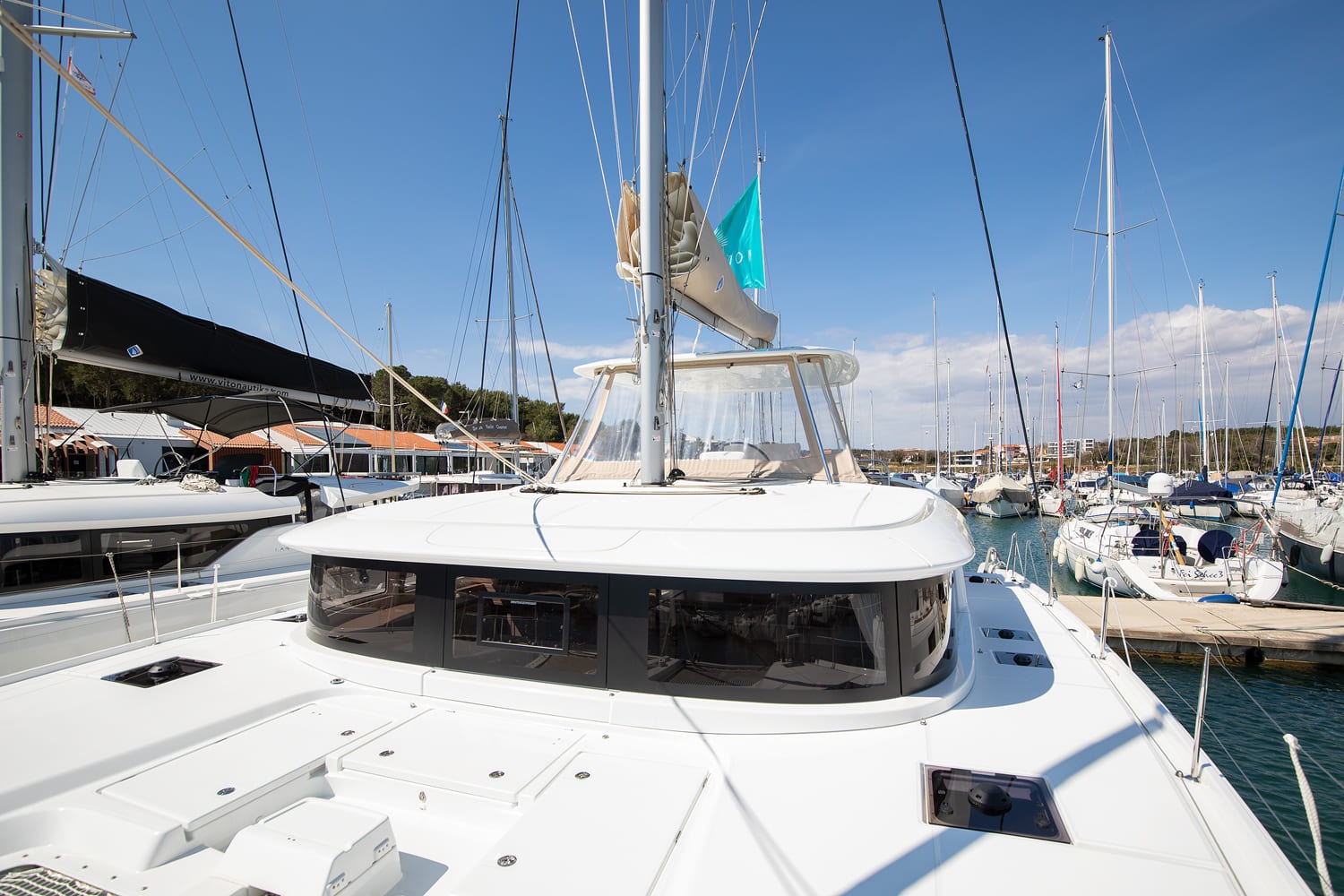 Coachroof and flybridge of the Lagoon 46 seen from the foredeck, with tinted saloon windows, mast, boom and courtesy flag