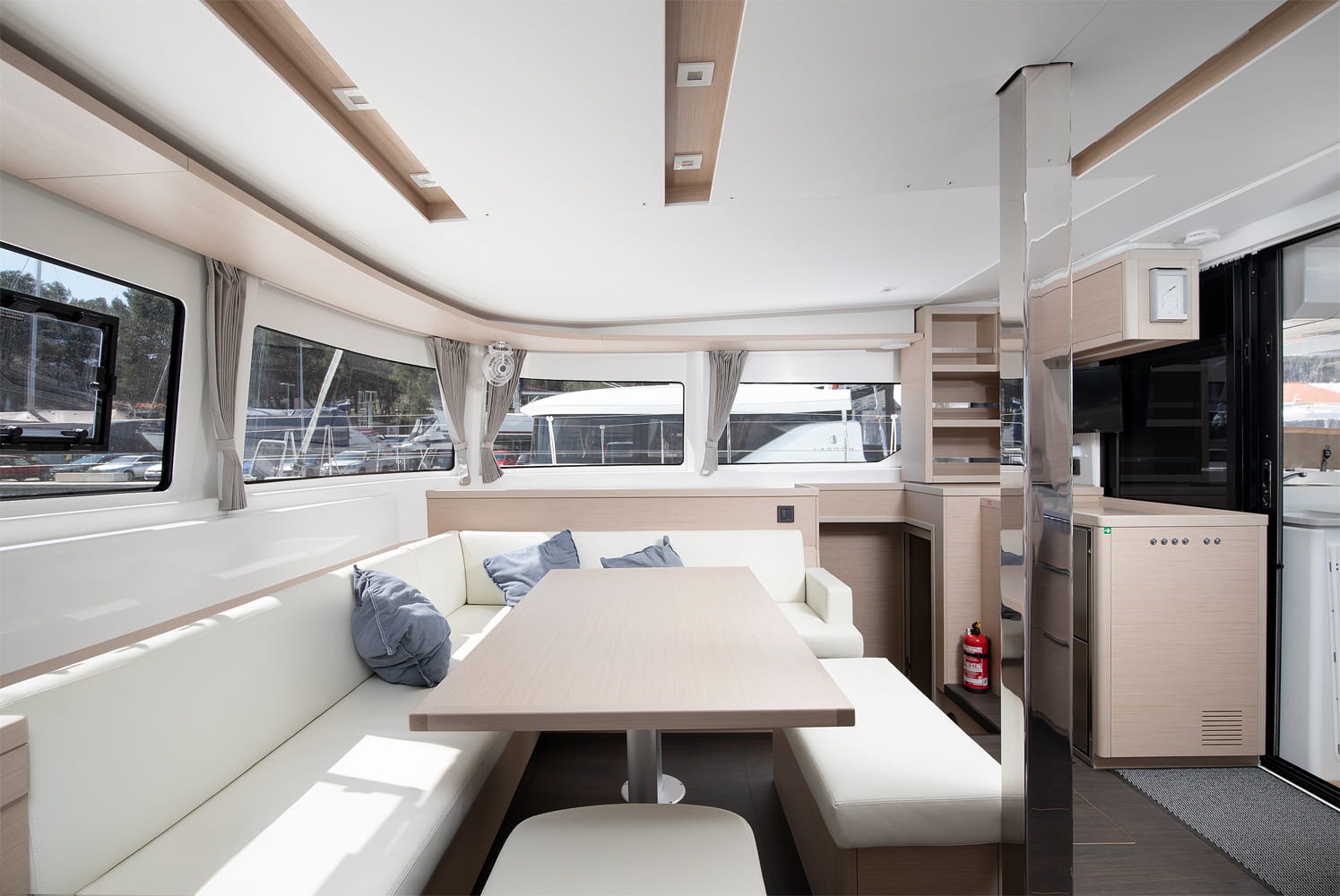 Saloon dining area of the Lagoon 46 with white upholstered settee, cushions, oak table, television and sliding door to the cockpit