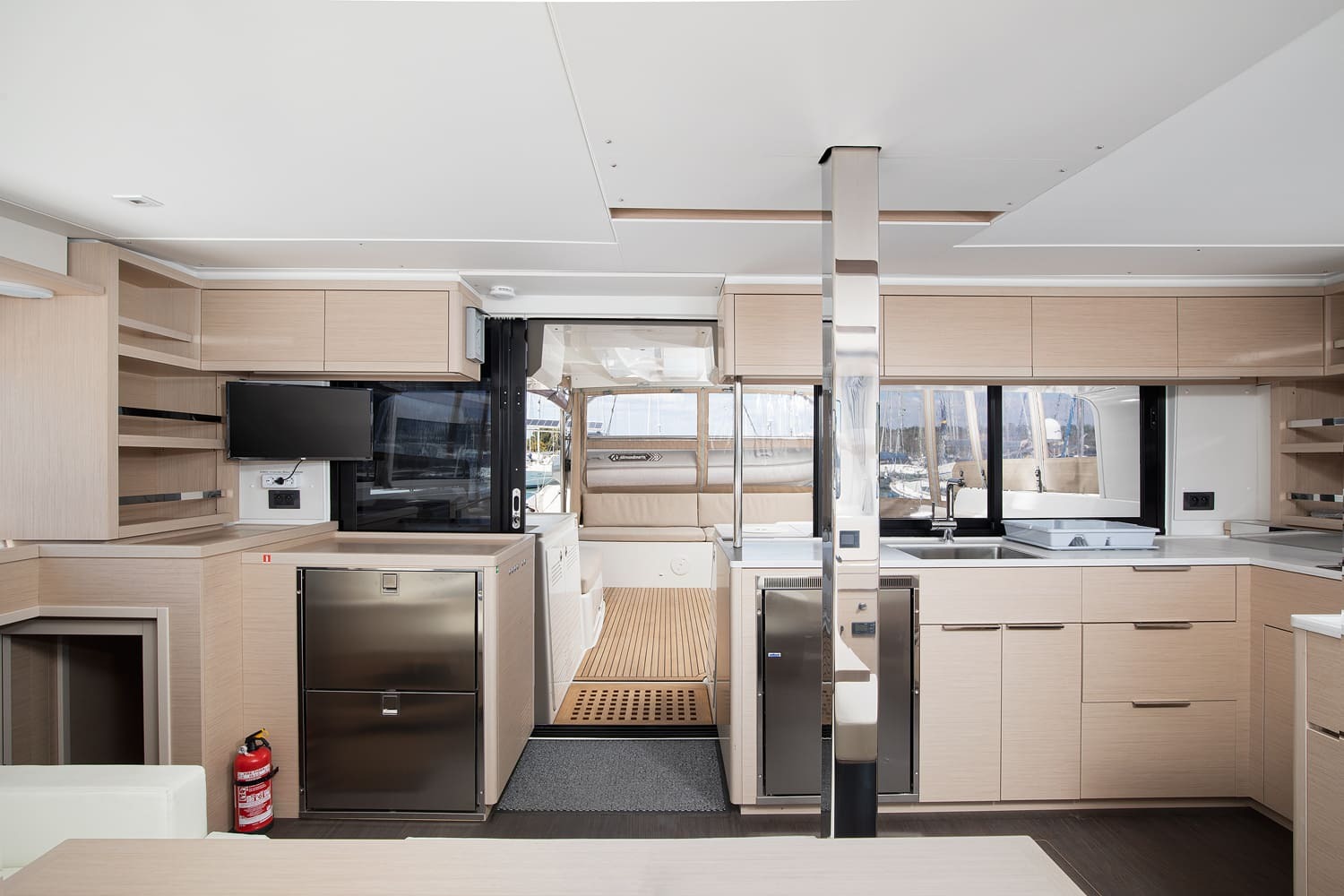 View aft through the Lagoon 46 saloon towards the cockpit, with two stainless fridge drawers, television and teak cockpit sole beyond