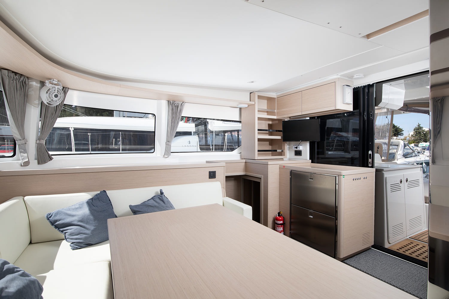 Saloon of the Lagoon 46 looking towards the galley, with dining table, fridge, television and open sliding door to the cockpit