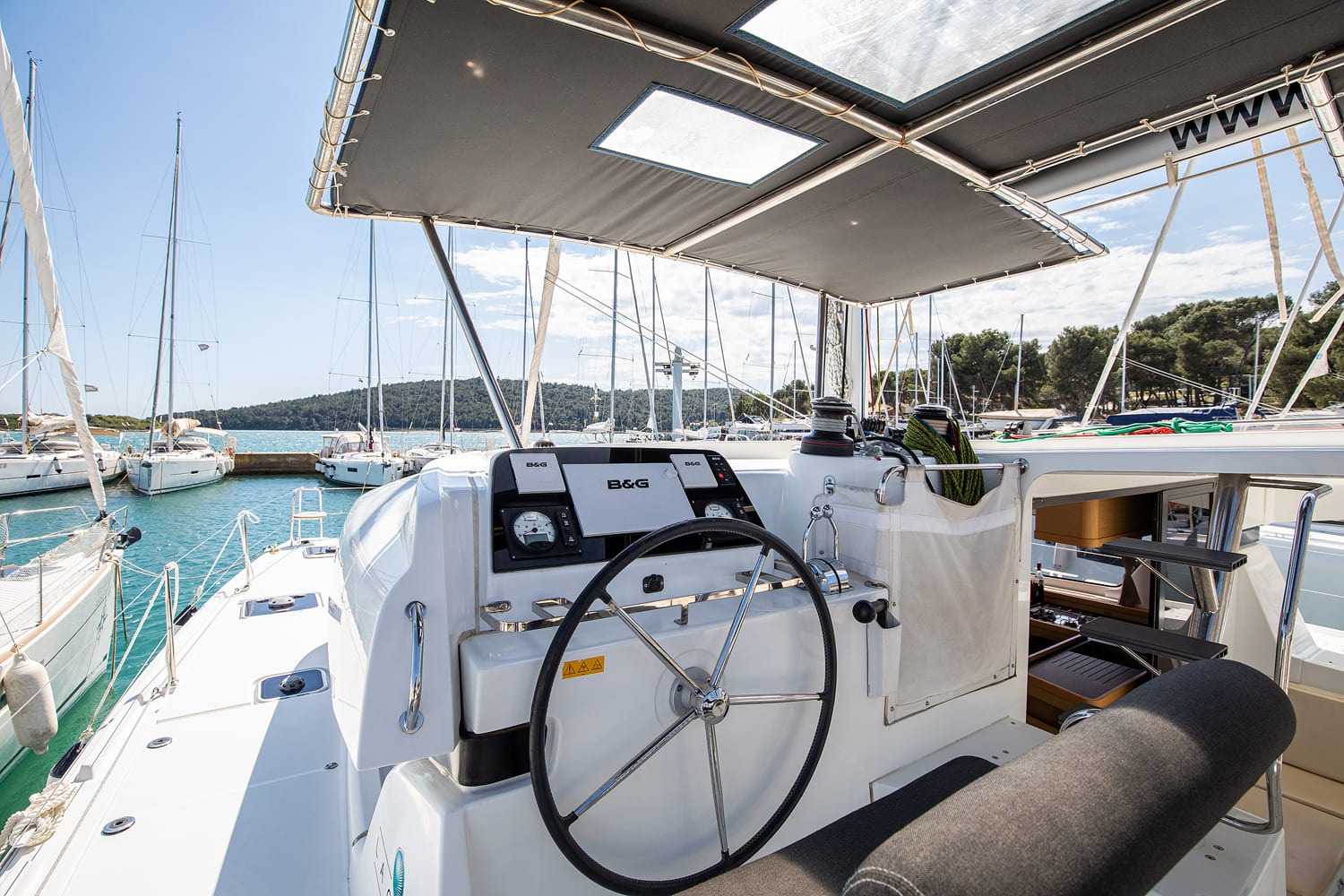 Starboard helm station under the bimini, with a stainless steering wheel and B&G instrument displays.