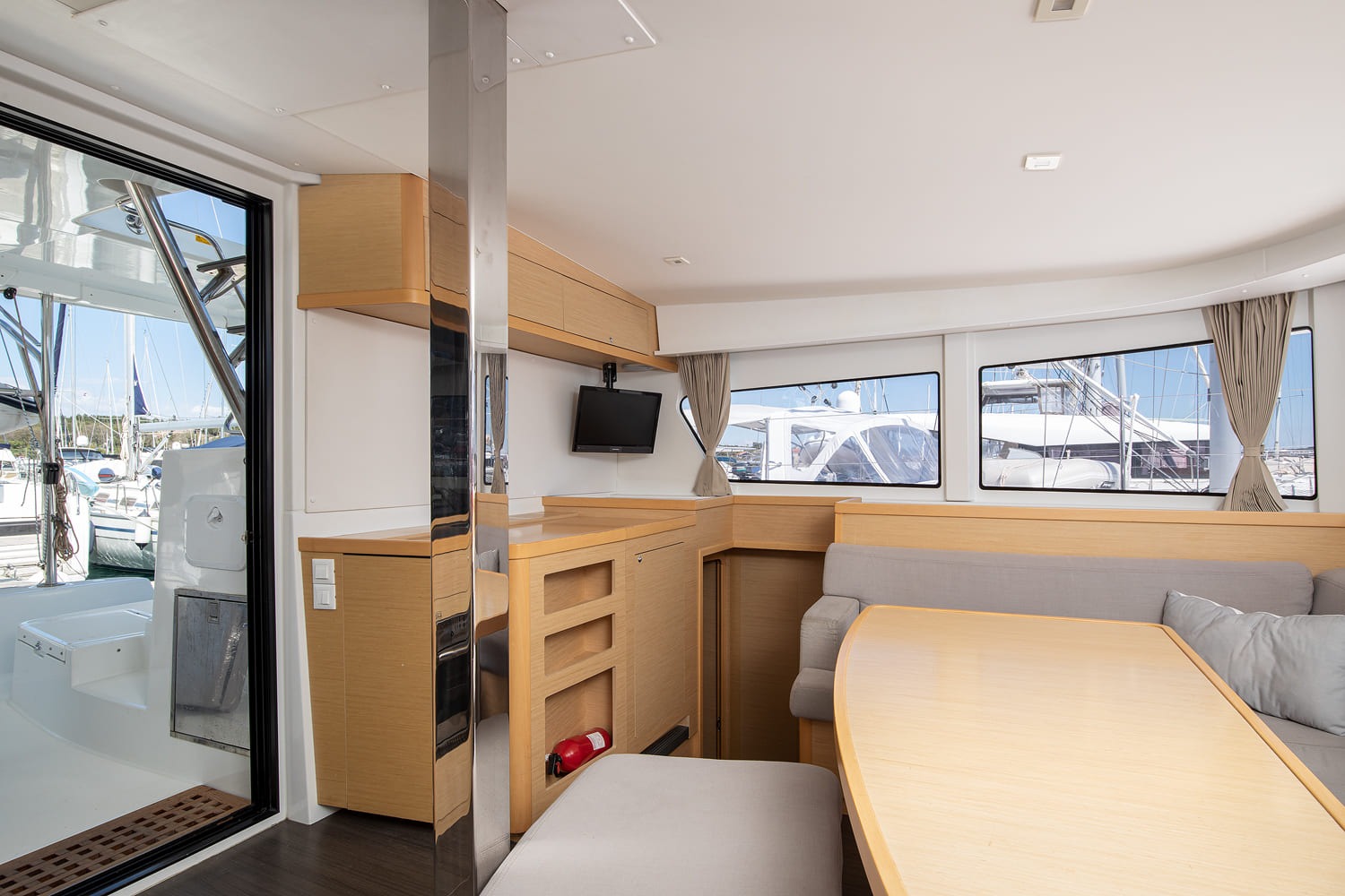 Saloon looking aft towards the sliding glass door to the cockpit, with a wall-mounted television and overhead lockers.