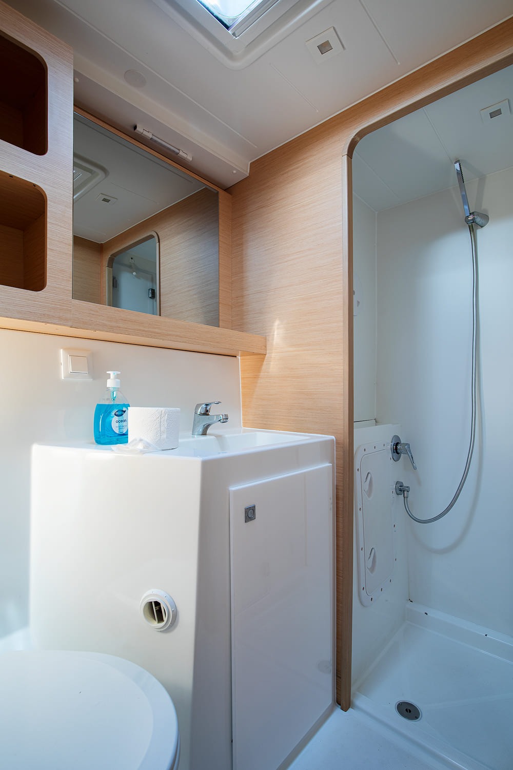 Heads with a separate shower stall, washbasin and mirror, lit by an overhead hatch.