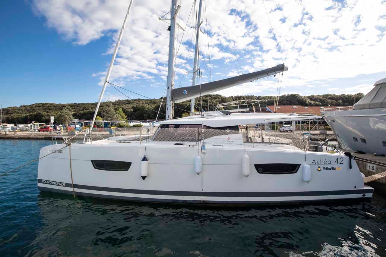 Follow the Sun, a Fountaine Pajot Astrea 42 catamaran, moored alongside a pontoon with her white hulls and boom cover visible in the afternoon sun.