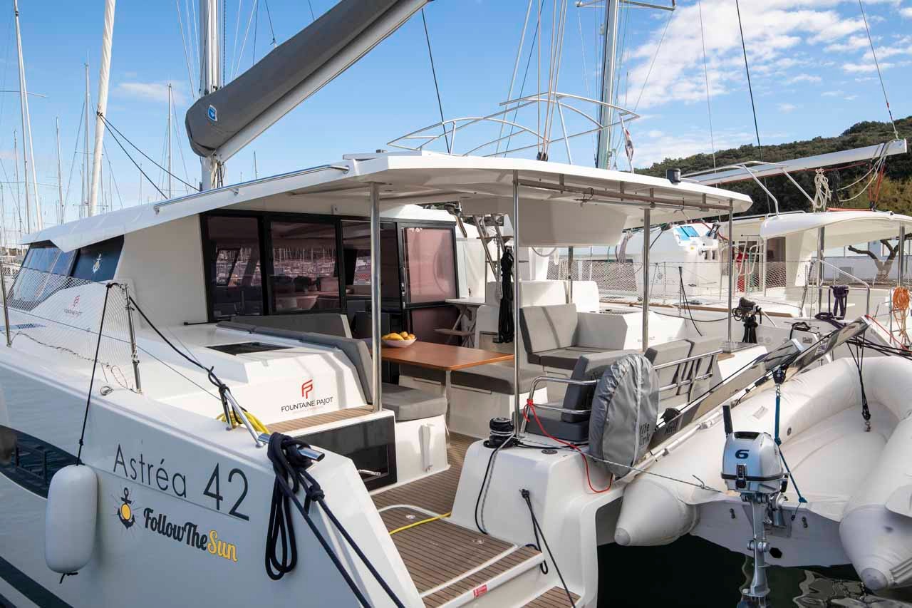 The aft cockpit of Follow the Sun seen from the quarter, with teak decking, a dining table and the tender hanging on davits.