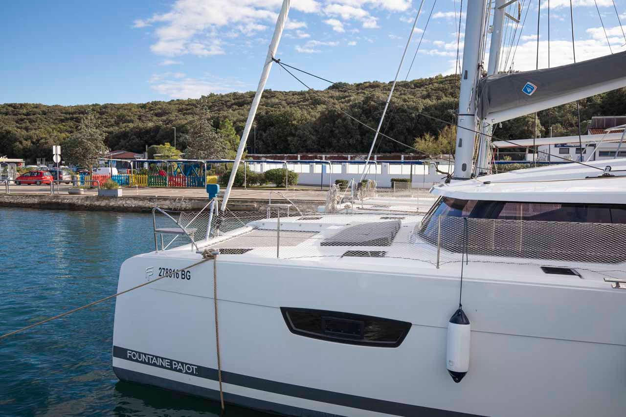 The bow and trampoline of Follow the Sun seen from the pontoon, with the furled mainsail on the boom above.