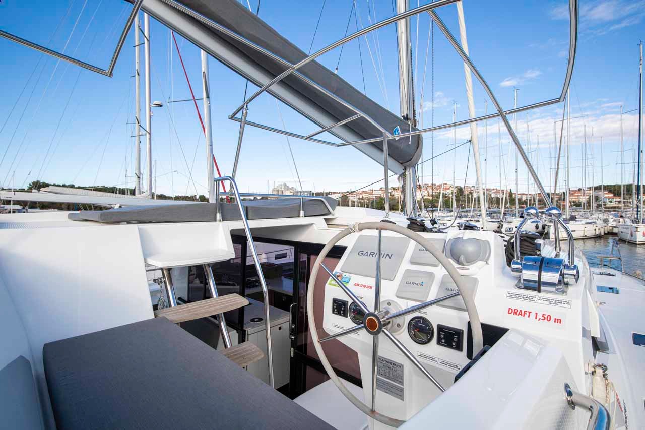 The helm station of Follow the Sun, with a stainless steering wheel, Garmin instrument displays and a clear view forward along the deck.