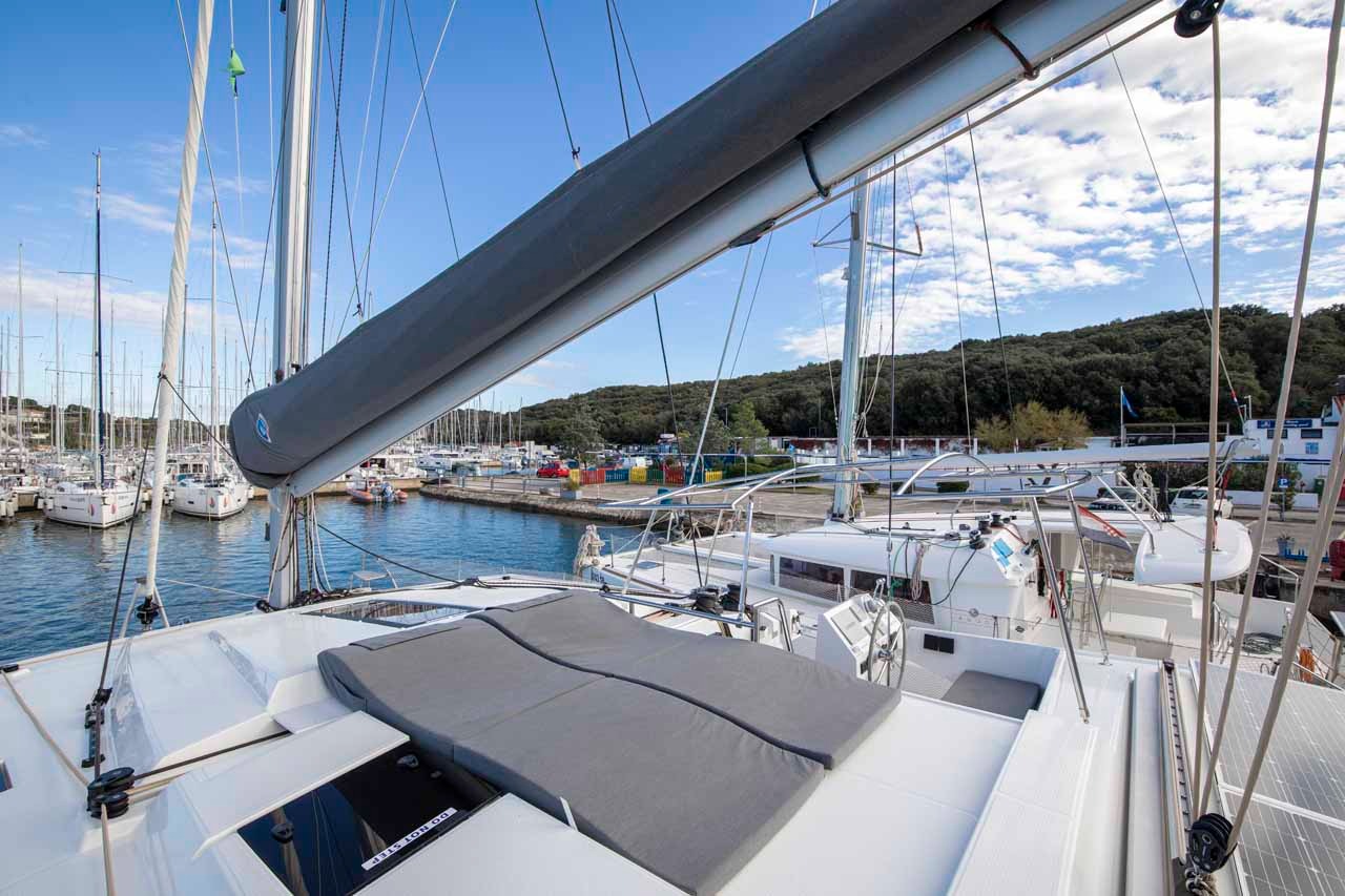 A padded sunbed on the foredeck of the Astrea 42, shaded by the boom and looking back over the pontoon.