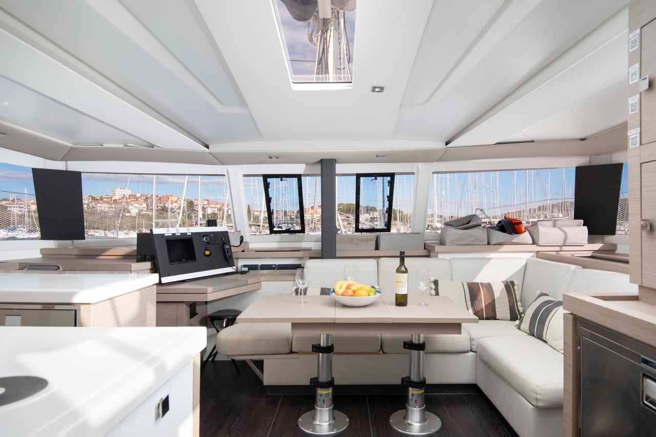 The saloon of the Astrea 42, with pale upholstered seating, a convertible dining table and panoramic windows on three sides.