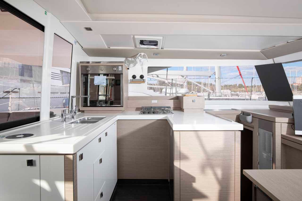 The galley of Follow the Sun, with a twin sink, gas hob, oven and generous worktop finished in light wood and white.
