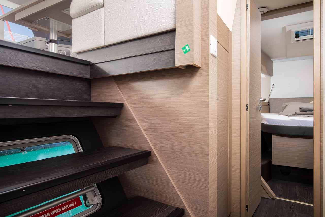The companionway steps leading down from the saloon into one of the hulls, with a cabin door open at the foot.