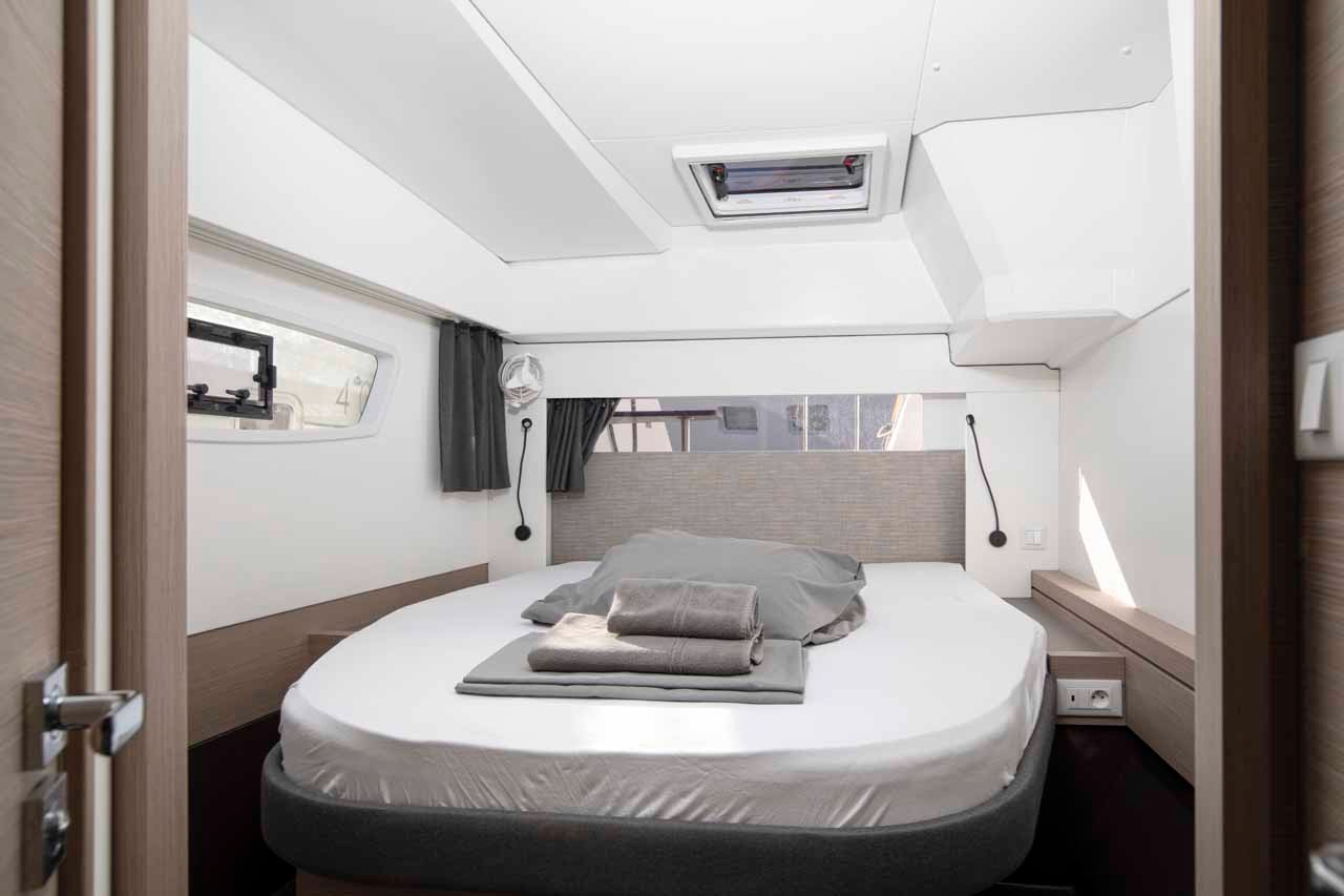 A bright double cabin in the Astrea 42, with a curtained hull window, reading lights and storage along the berth.