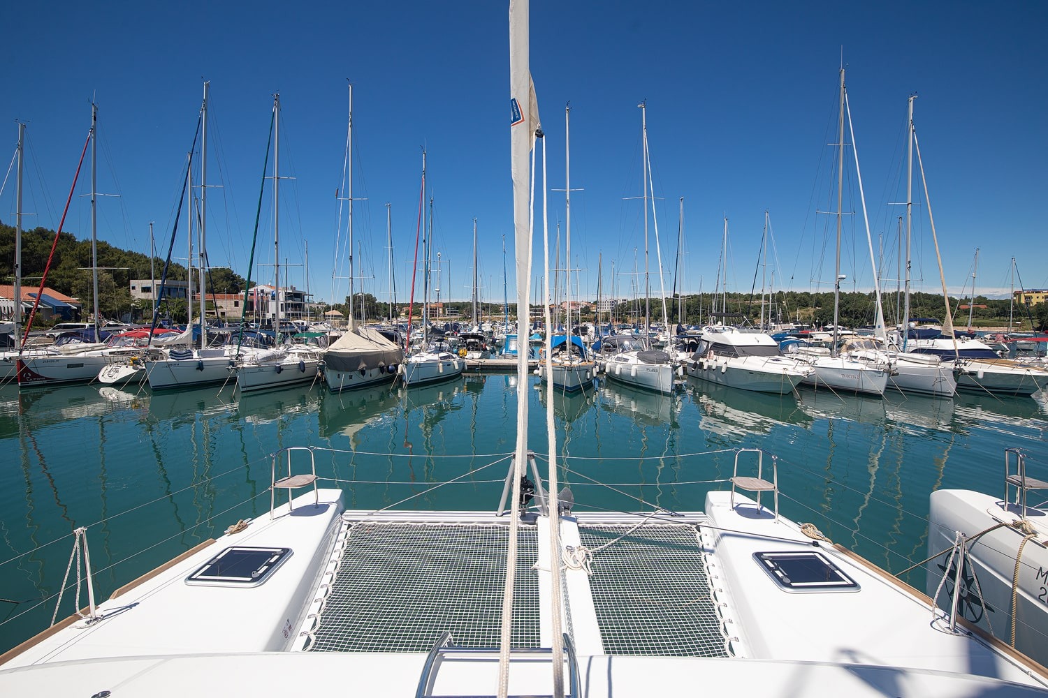 Foredeck of the Mare Ipanema looking forward over the trampoline between the two hulls, with the marina and moored yachts beyond