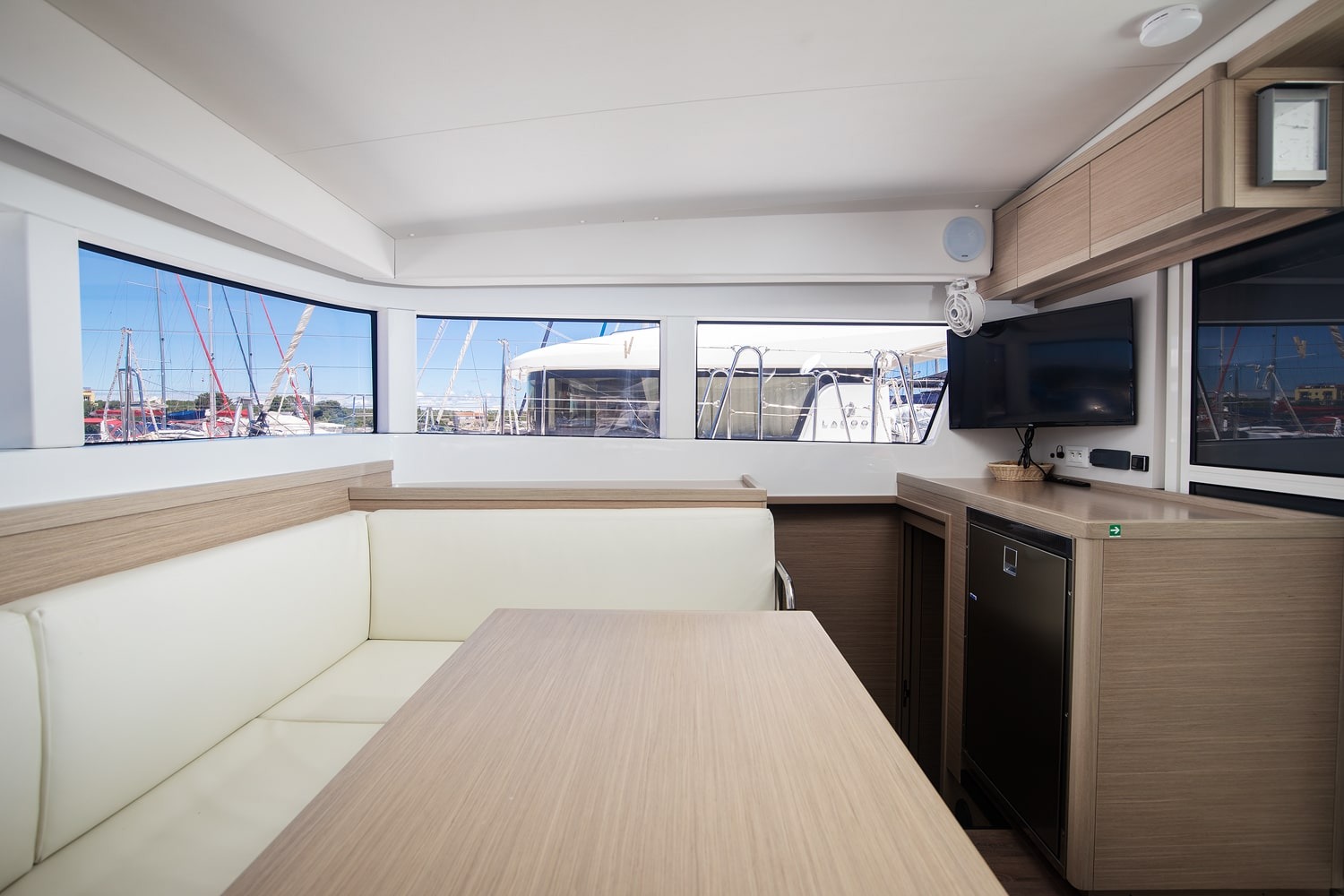 Saloon looking aft, with the dining settee, worktop, fridge and a flat screen television on the bulkhead
