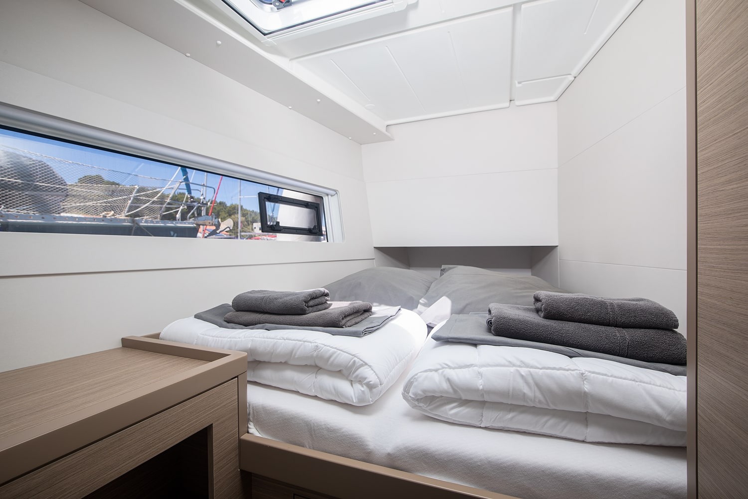 Double cabin in the hull with a made-up berth, folded towels, a hull window and an overhead hatch