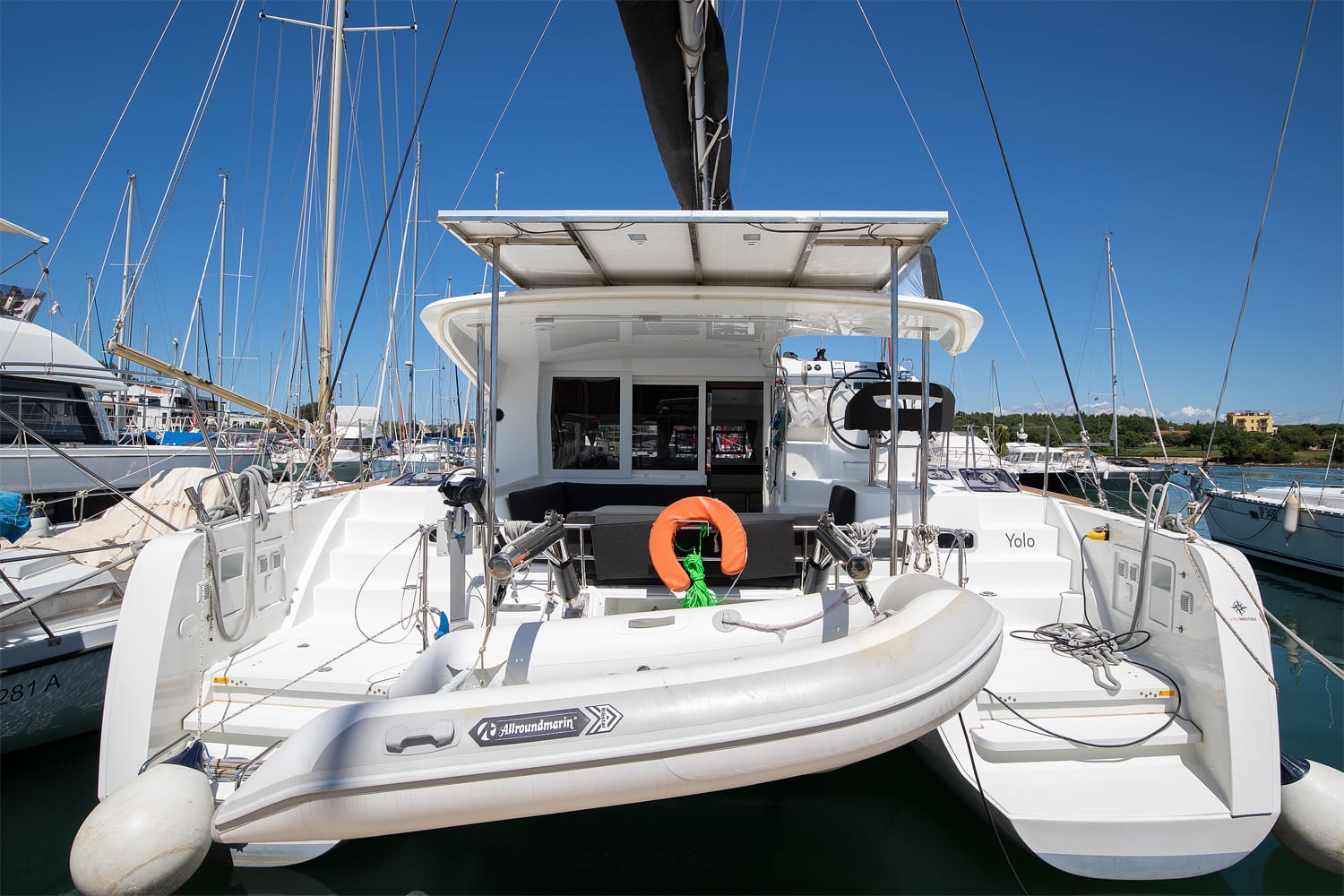 Stern view of the catamaran Yolo with the name on the transom, the tender on its davits and a lifebuoy in the cockpit.