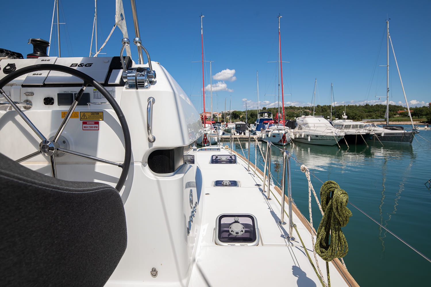 View forward along the side deck from the helm station, past the deck hatches to the boats moored across the marina.