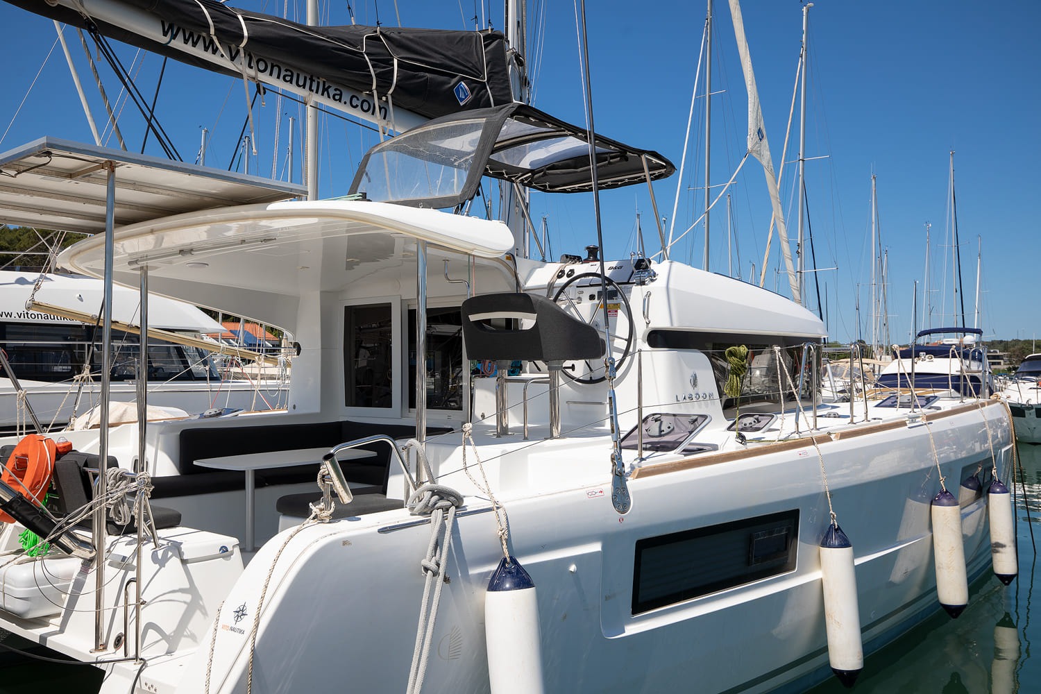 Lagoon 40 catamaran Yolo moored in ACI Marina Pomer, seen from the side with the shaded cockpit, helm seat and fenders along the hull.