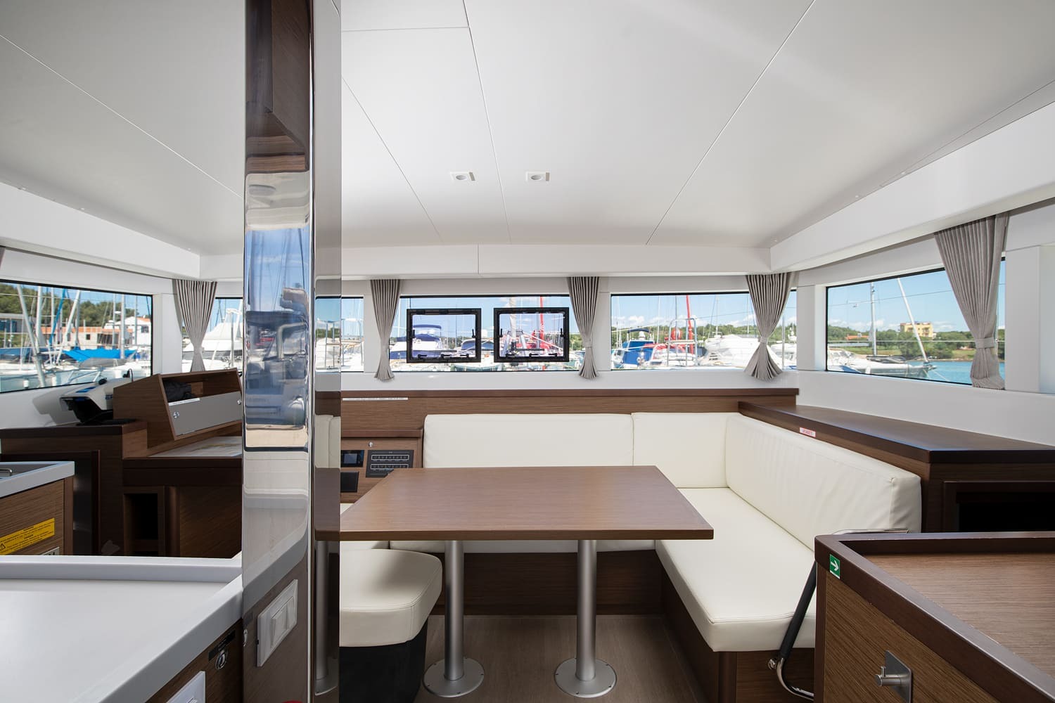 Saloon dining area with a cream L-shaped settee, wooden table and panoramic windows looking out over the marina.