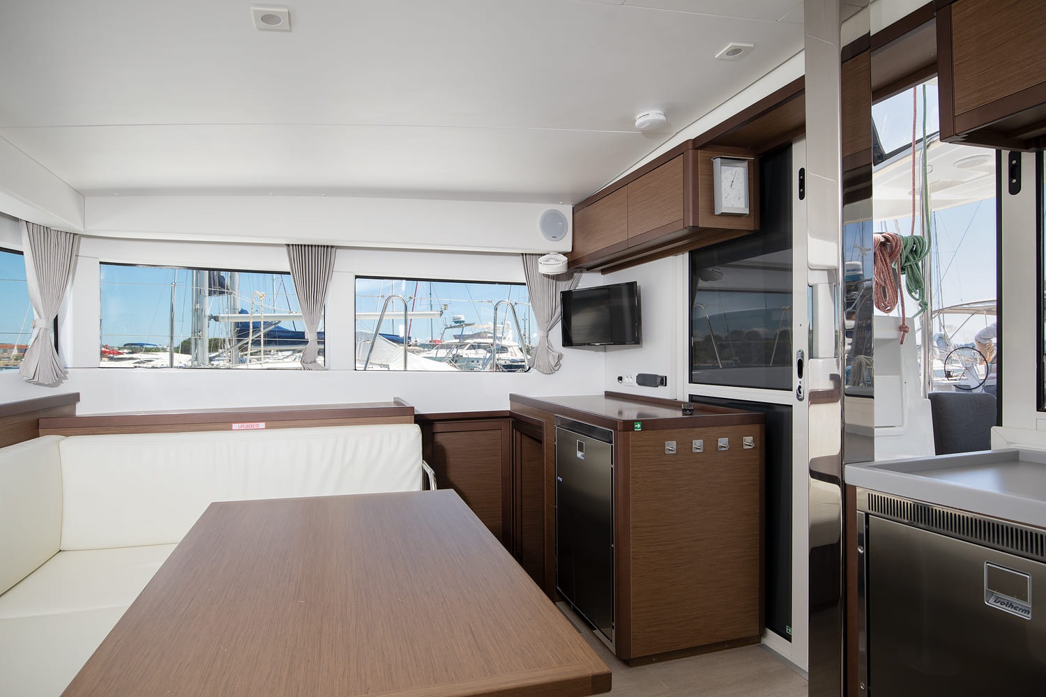Saloon with dining table, fridge unit and wall-mounted television, and the door out to the cockpit.