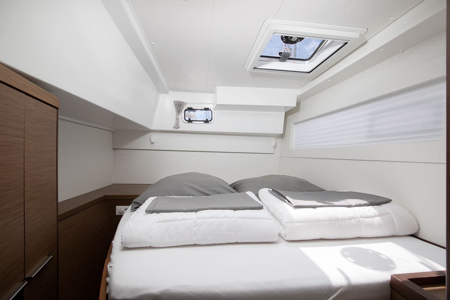 Double cabin with the berth made up in white linen, an overhead hatch, opening portlight and wardrobe to the left.