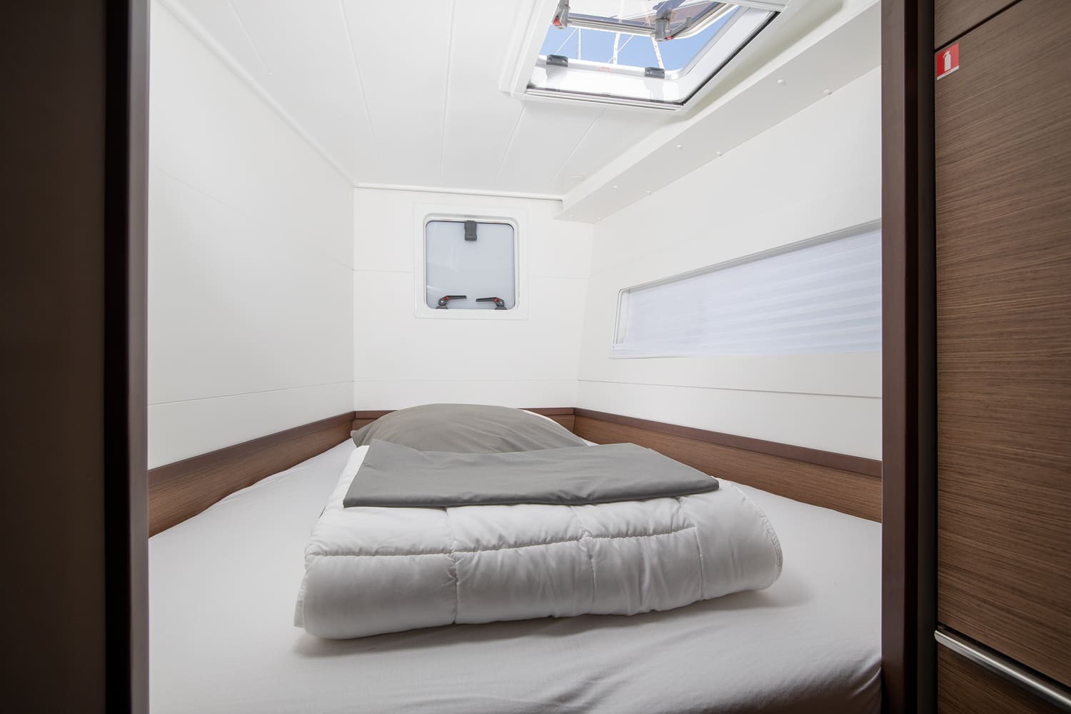 Cabin seen from the doorway, with a made-up double berth, hatch overhead and a portlight in the bulkhead.