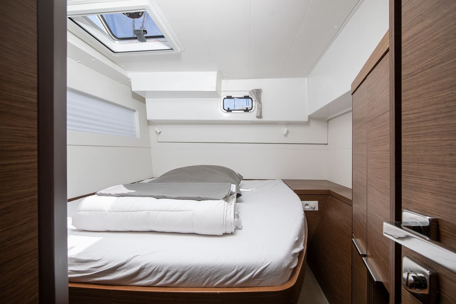 Double cabin with white bedding, wardrobe to the right, an overhead hatch and a portlight above the berth.