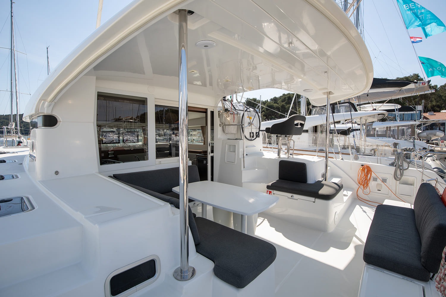 Foredeck and coachroof of the Lagoon 40 seen from the bow, with trampoline netting, deck hatches and Vito Nautika flags on the yachts behind