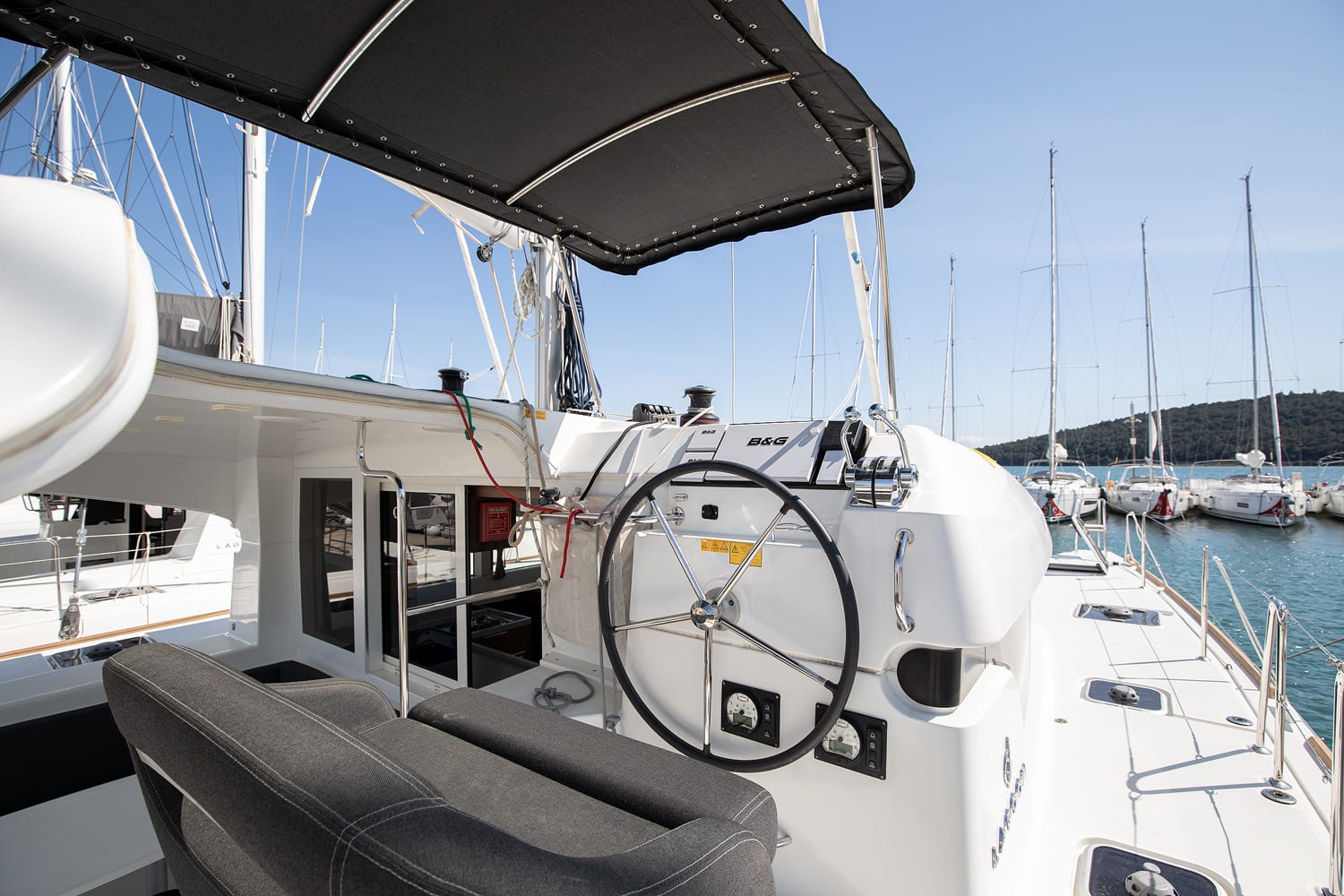 Cockpit seen from aft, with L-shaped bench, table and helm station, a neighbouring Lagoon catamaran alongside