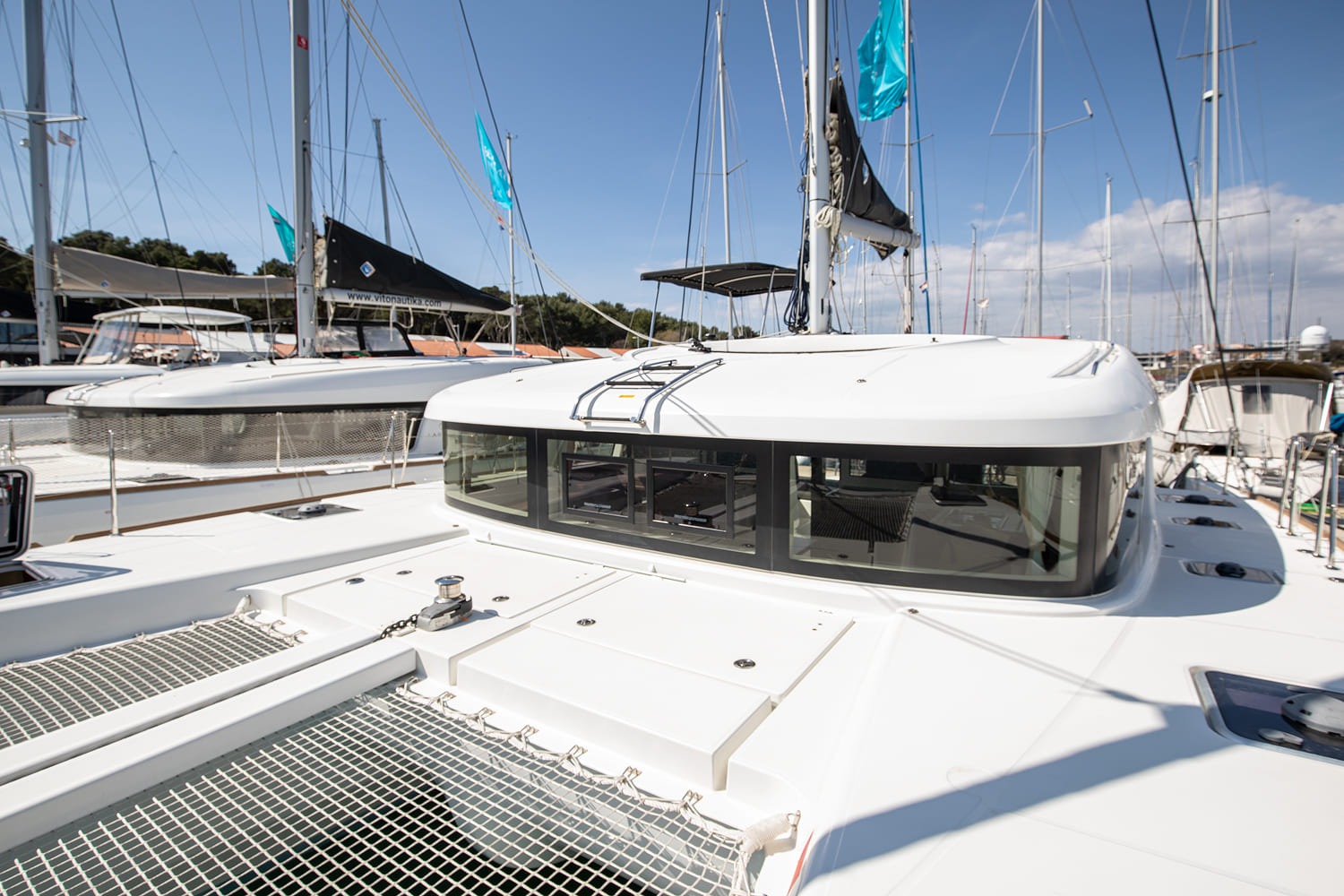 Helm station with B&G instruments and wheel under a black bimini, looking forward along the starboard side deck