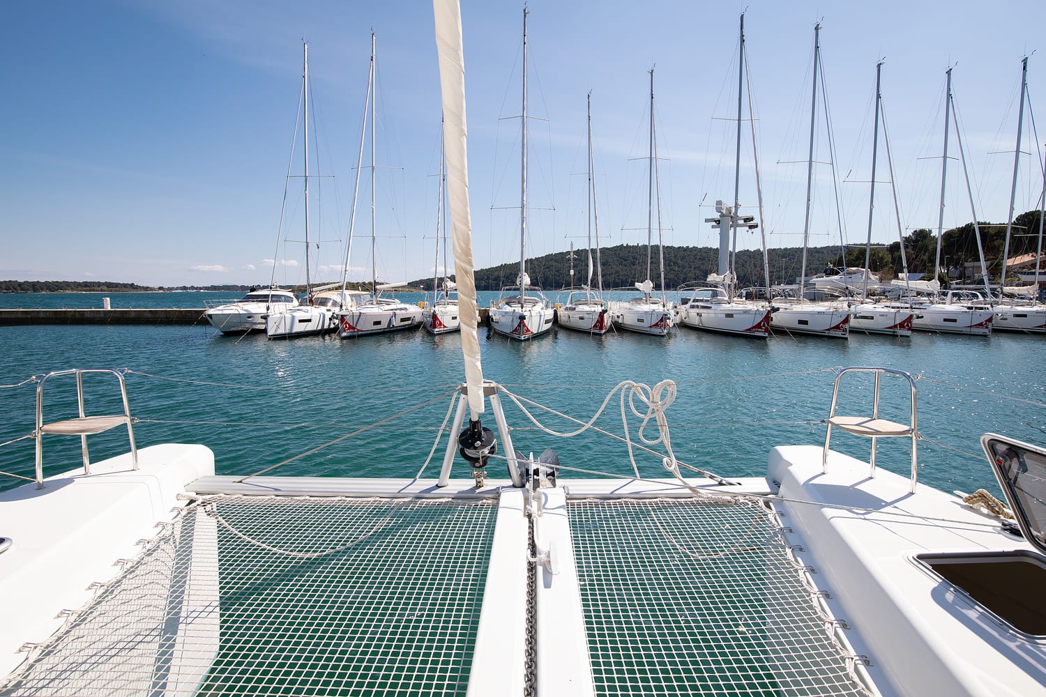 View forward from the foredeck across the trampolines to the pontoon and moored yachts in Pomer bay