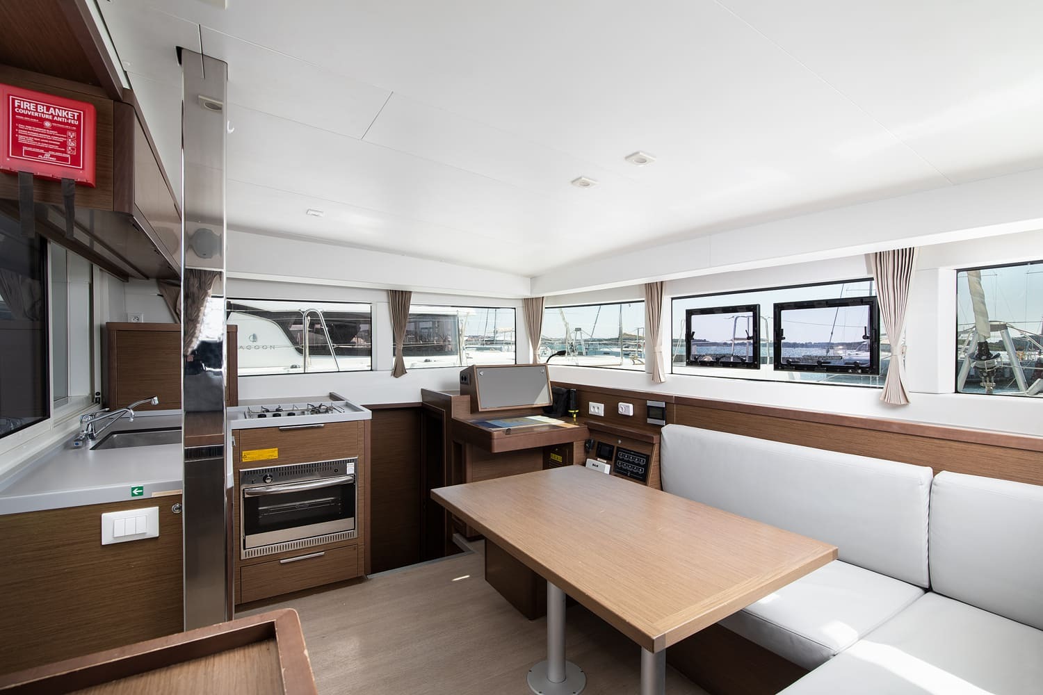 Saloon with galley, gas hob and oven, chart table, dining table and white settee below panoramic windows