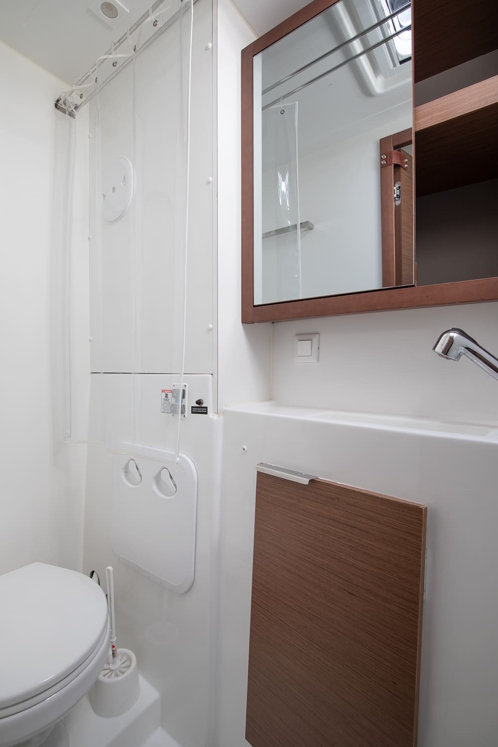 Heads compartment with electric toilet, sink, mirrored cabinet and shower curtain below the deck hatch