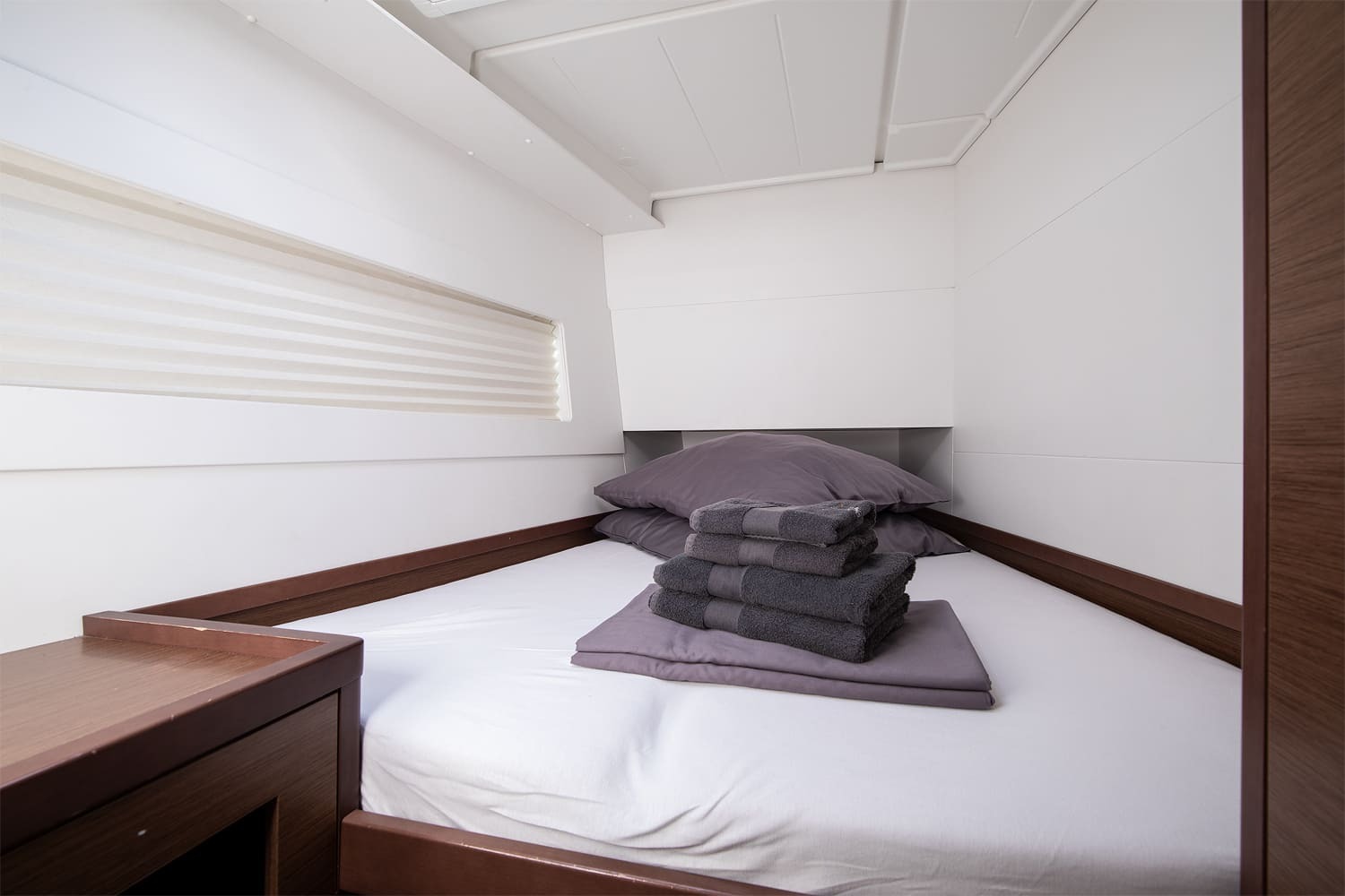 Double cabin with made-up berth, folded towels and a pleated blind over the hull window