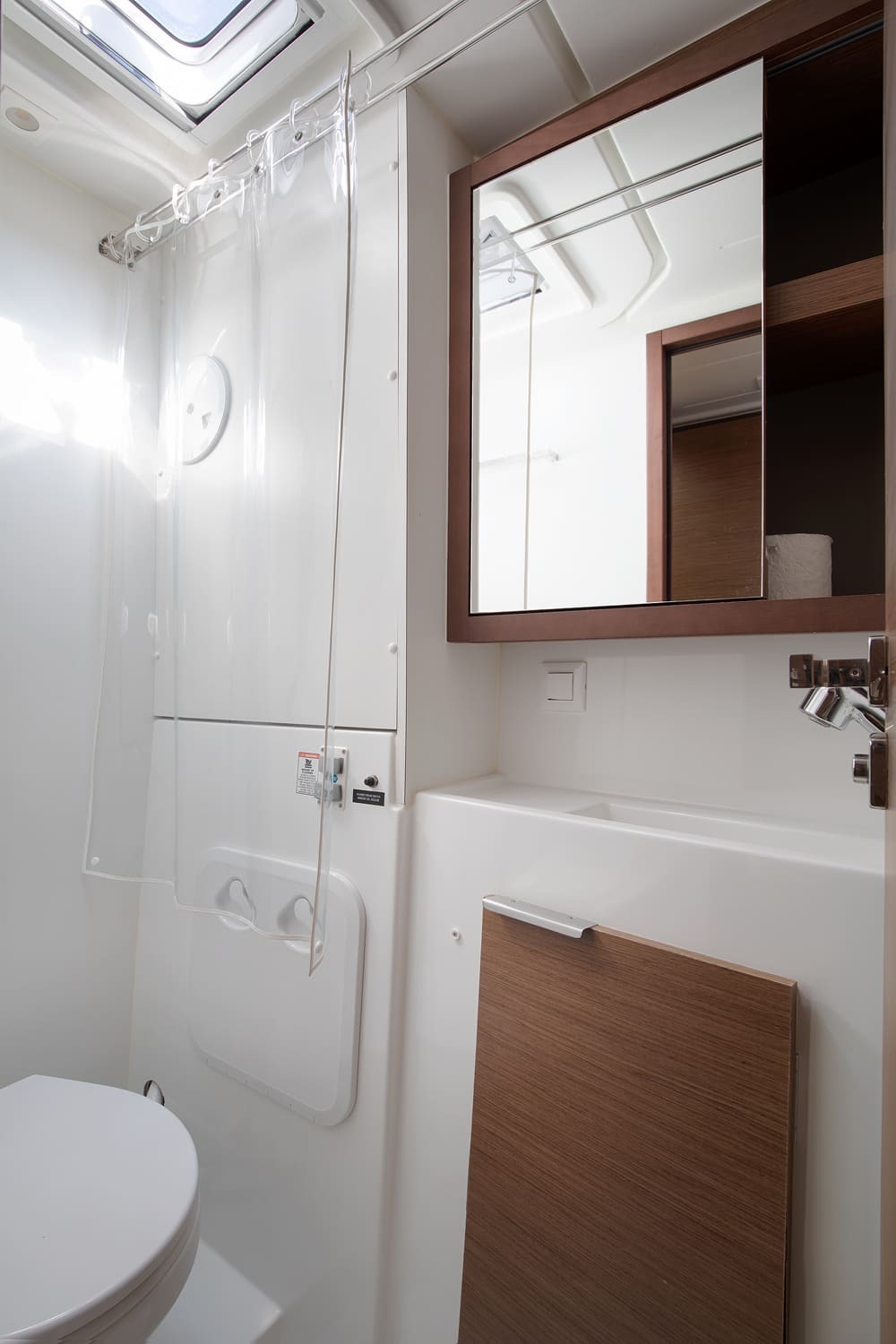 Heads with electric toilet, sink and mirrored cabinet, shower curtain drawn back below the hatch