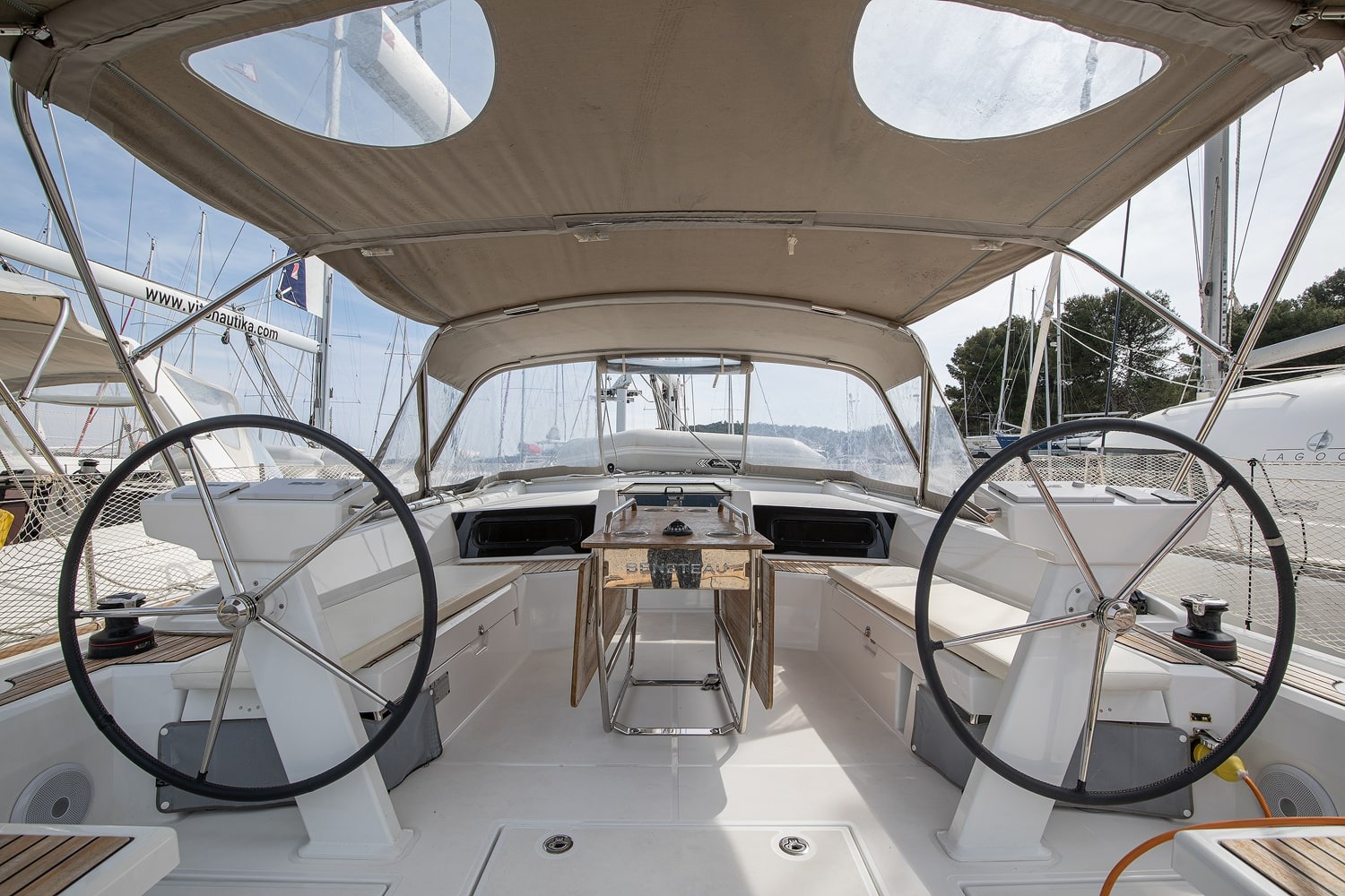 The cockpit of Amore di Mare under its bimini top, with twin wheels, folding table and teak seating