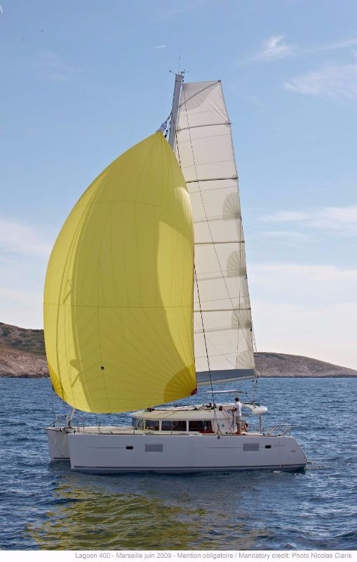 Lagoon 400 catamaran sailing under a yellow gennaker past a bare rocky islet