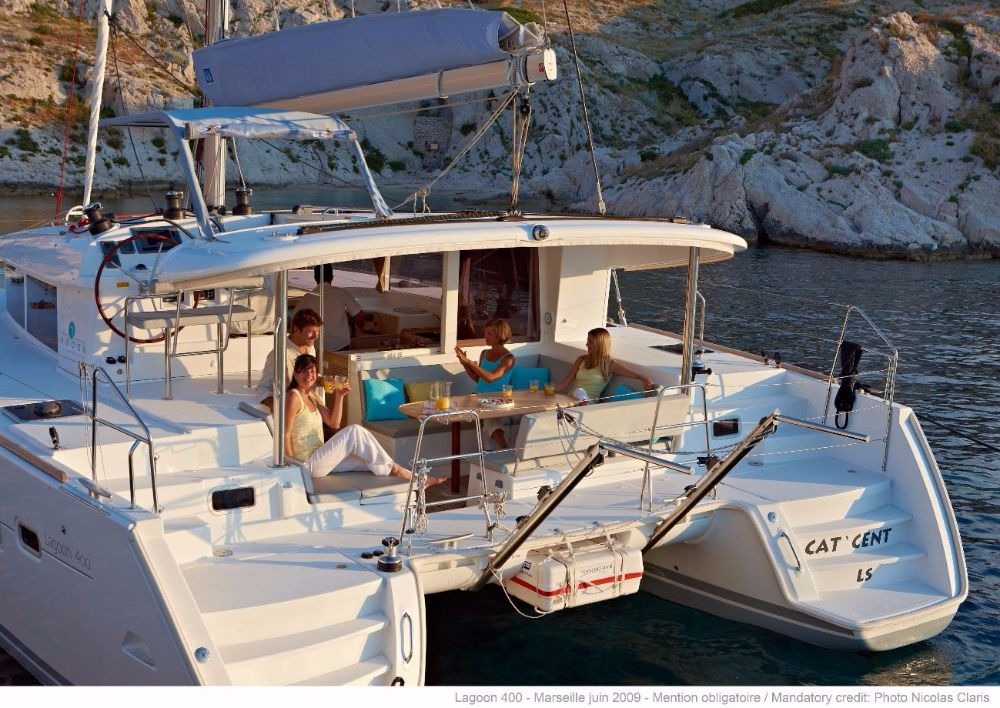 Cockpit of a Lagoon 400 catamaran at anchor, with people around the table under the bimini and the saloon doors open behind