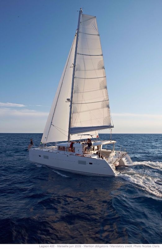 Lagoon 400 catamaran sailing under full main and genoa on open blue water, seen from ahead with crew on deck