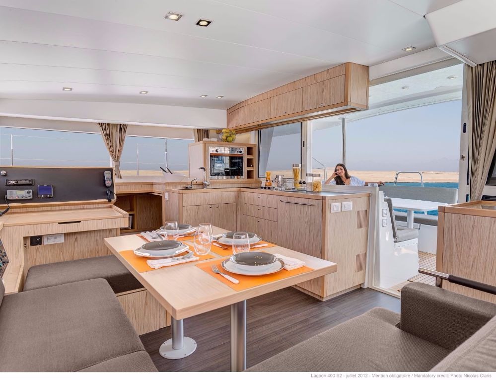 Saloon of a Lagoon 400 catamaran with the table set for four, the galley to the right and the navigation station on the left