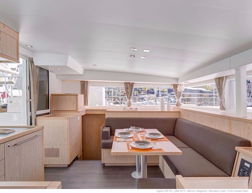 Dining area of a Lagoon 400 catamaran with an L-shaped settee, set table and panoramic windows along the saloon