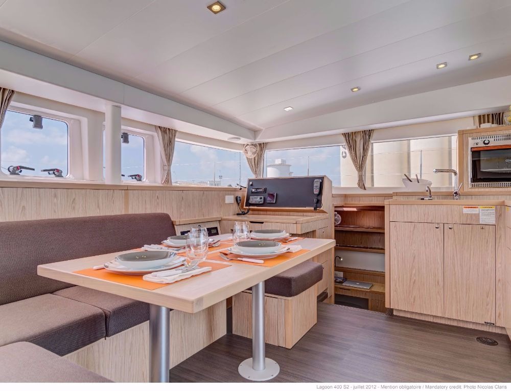 Saloon of a Lagoon 400 catamaran seen from the settee, with the set dining table, navigation station and galley with sink and microwave