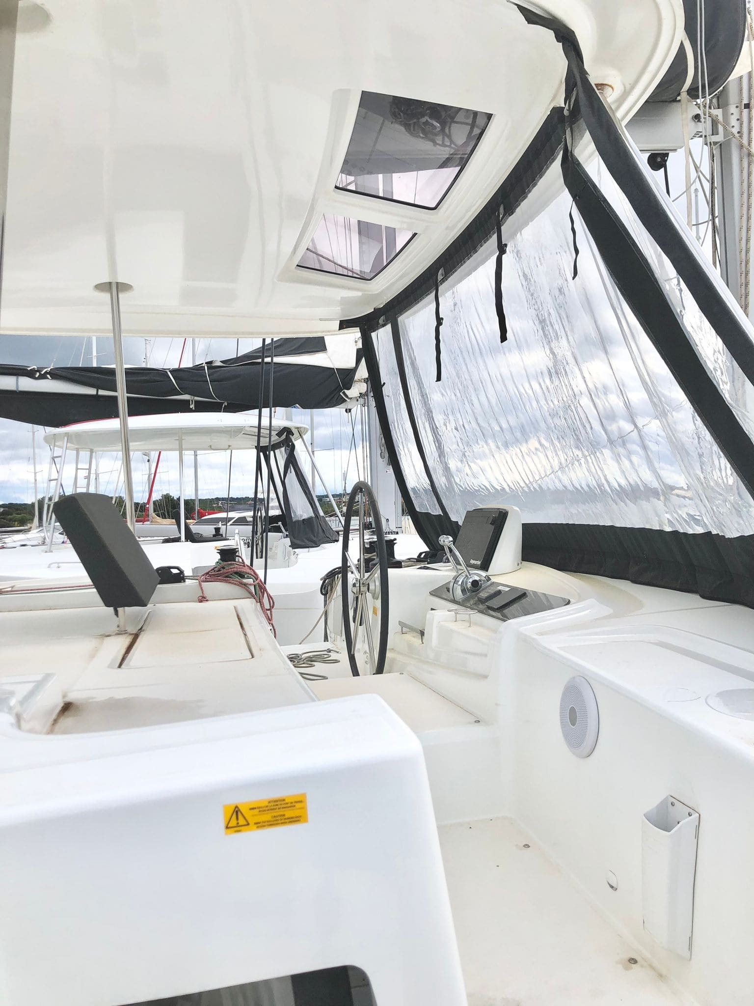 Helm station of the Lagoon 46 Venice Beach under the flybridge, with steering wheel, throttle controls and clear cockpit enclosure