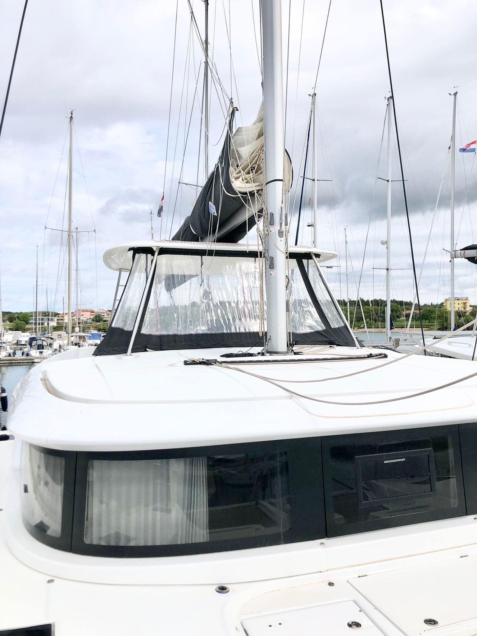 Foredeck and mast of the Lagoon 46 Venice Beach, with stowed mainsail, coachroof windows and marina masts behind